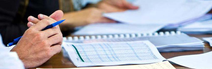 Hands holding a pen resting on a desk with a selection of documents